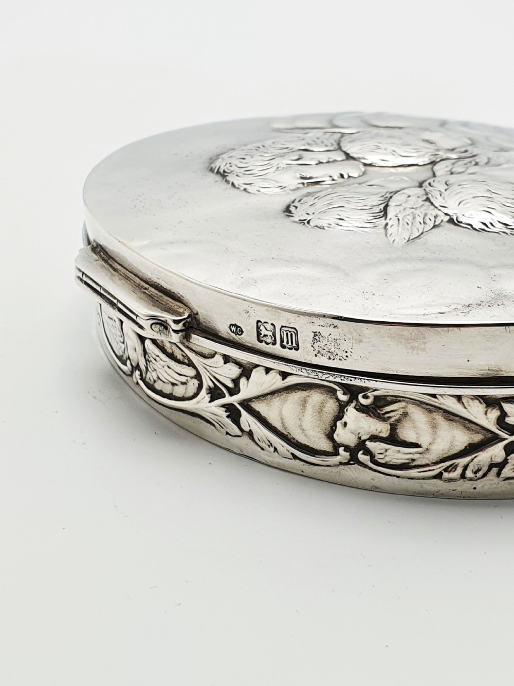 An oval sterling silver trinket box featuring an embossed lid with four cherub heads and a foliate border along the rim. View VI