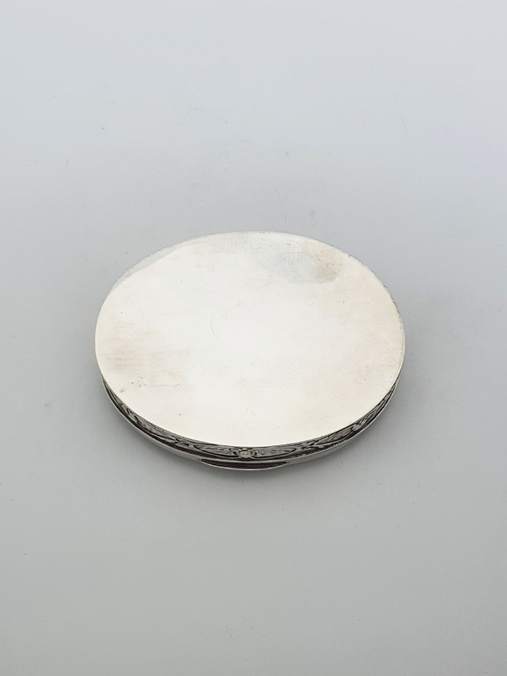 An oval sterling silver trinket box featuring an embossed lid with four cherub heads and a foliate border along the rim. View VIII