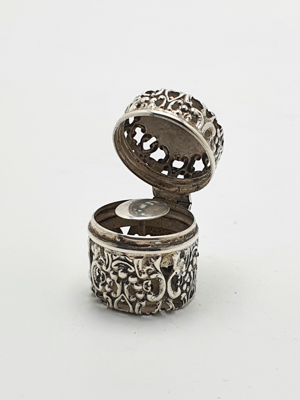 A small cylindrical sterling silver cotton holder featuring intricate pierced floral scrollwork and an open hinged lid displaying an internal thread post.