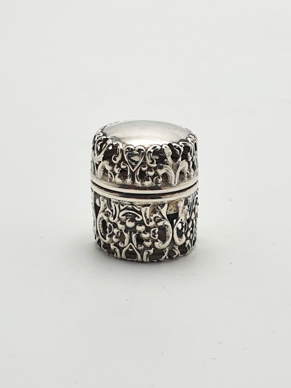 A small cylindrical sterling silver cotton holder featuring intricate pierced floral scrollwork and an open hinged lid displaying an internal thread post. View II