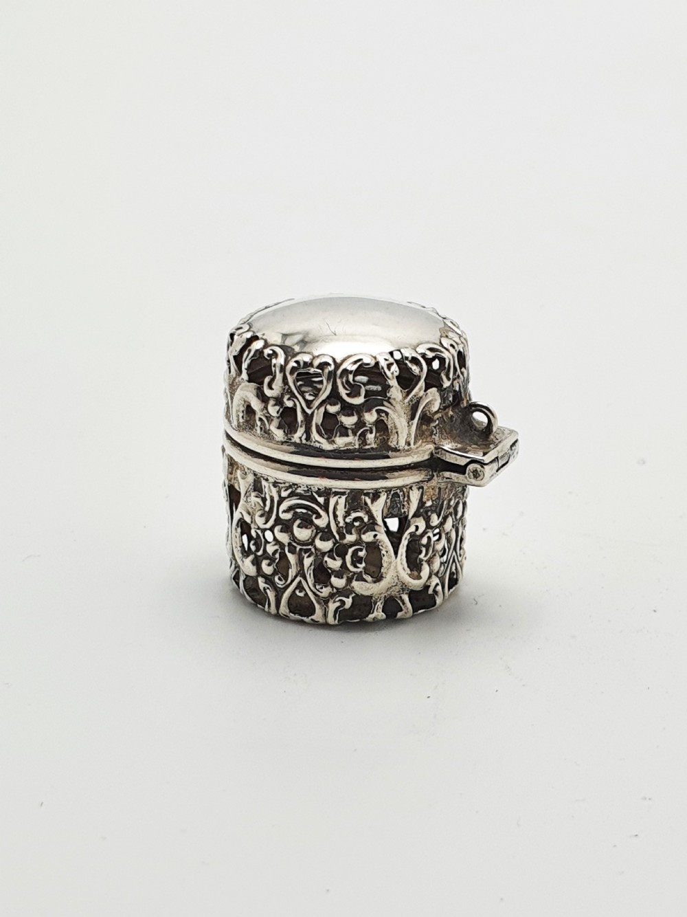 A small cylindrical sterling silver cotton holder featuring intricate pierced floral scrollwork and an open hinged lid displaying an internal thread post. View III