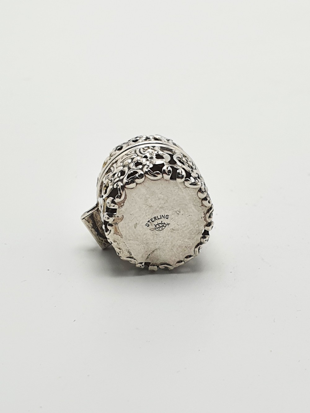 A small cylindrical sterling silver cotton holder featuring intricate pierced floral scrollwork and an open hinged lid displaying an internal thread post. View V