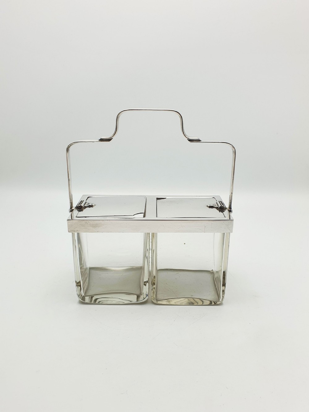 An antique silver-plated metal stand holding two clear rectangular glass jars with a central handle and mechanical lid system. View II