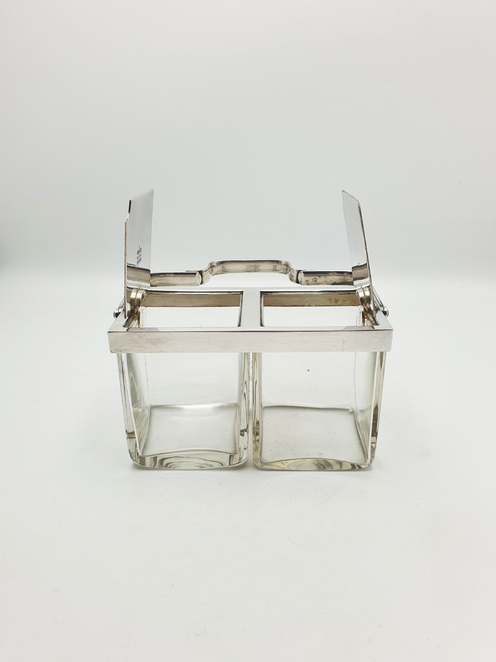 An antique silver-plated metal stand holding two clear rectangular glass jars with a central handle and mechanical lid system. View III