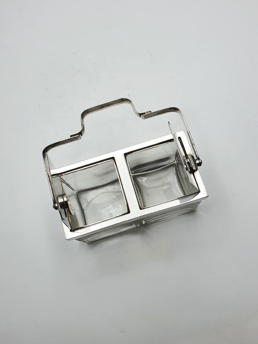 An antique silver-plated metal stand holding two clear rectangular glass jars with a central handle and mechanical lid system. View X
