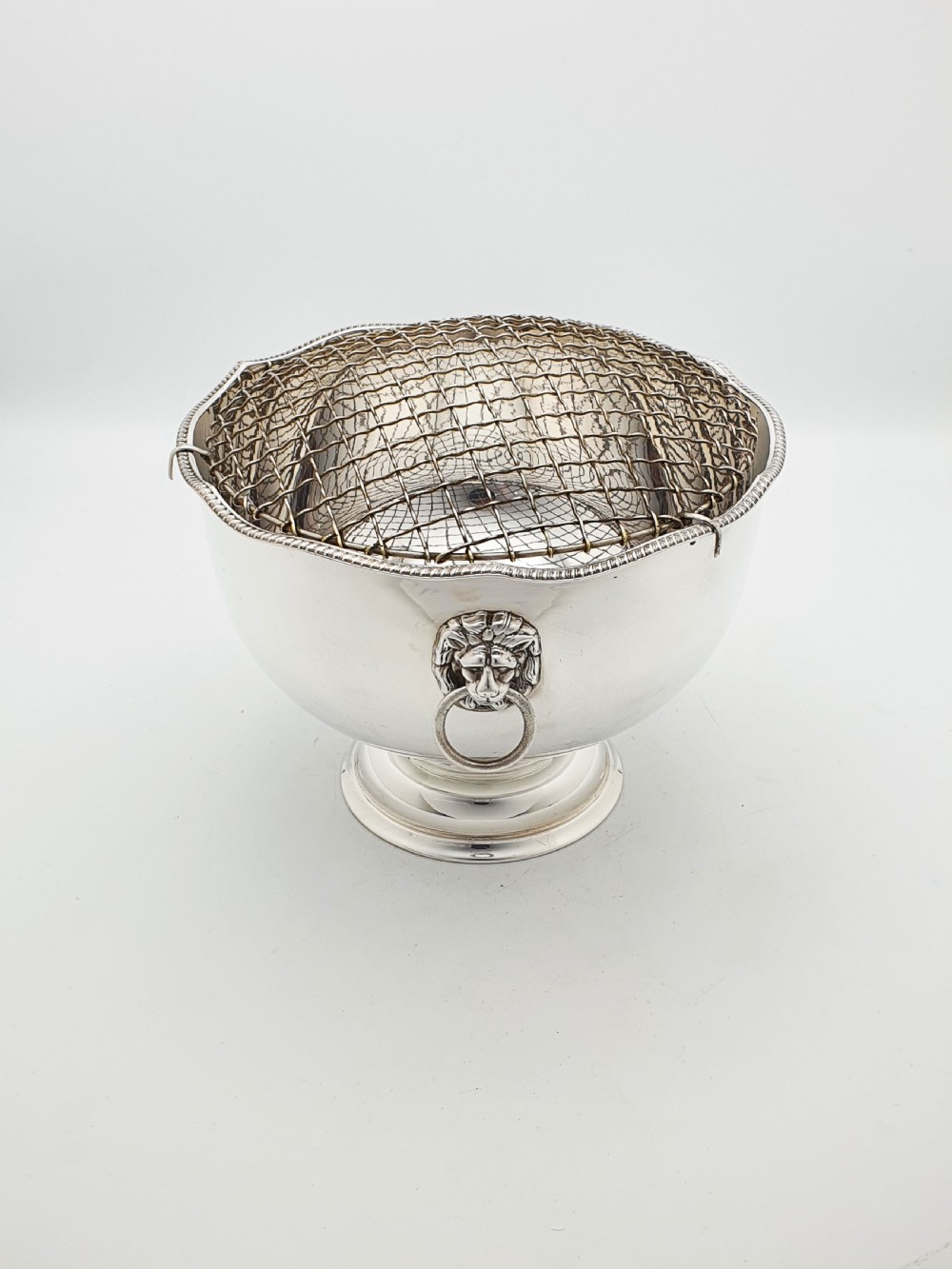 A circular silver-plated rose bowl featuring lion mask ring handles, a stepped pedestal base, and a removable wire mesh grid insert. View III