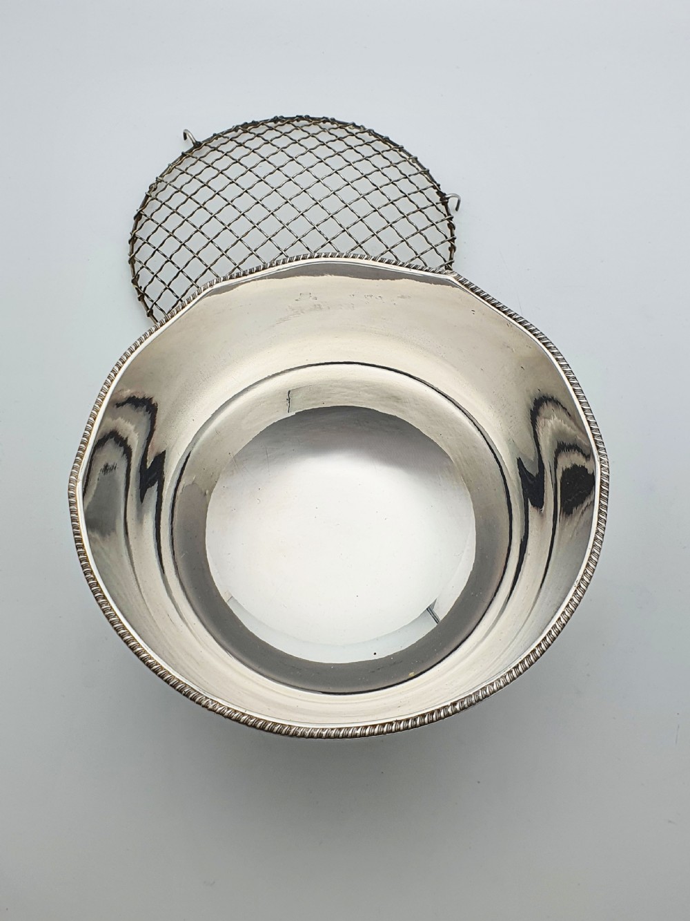 A circular silver-plated rose bowl featuring lion mask ring handles, a stepped pedestal base, and a removable wire mesh grid insert. View VIII