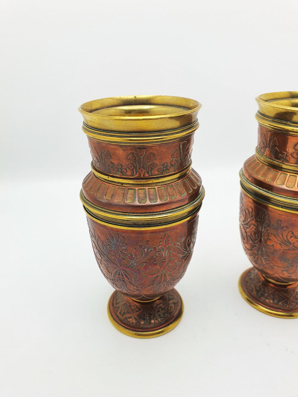 A pair of antique French copper urns featuring brass rims, pedestal bases, and chased floral motifs. View II