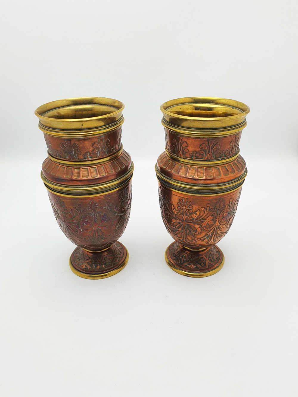 A pair of antique French copper urns featuring brass rims, pedestal bases, and chased floral motifs. View VI