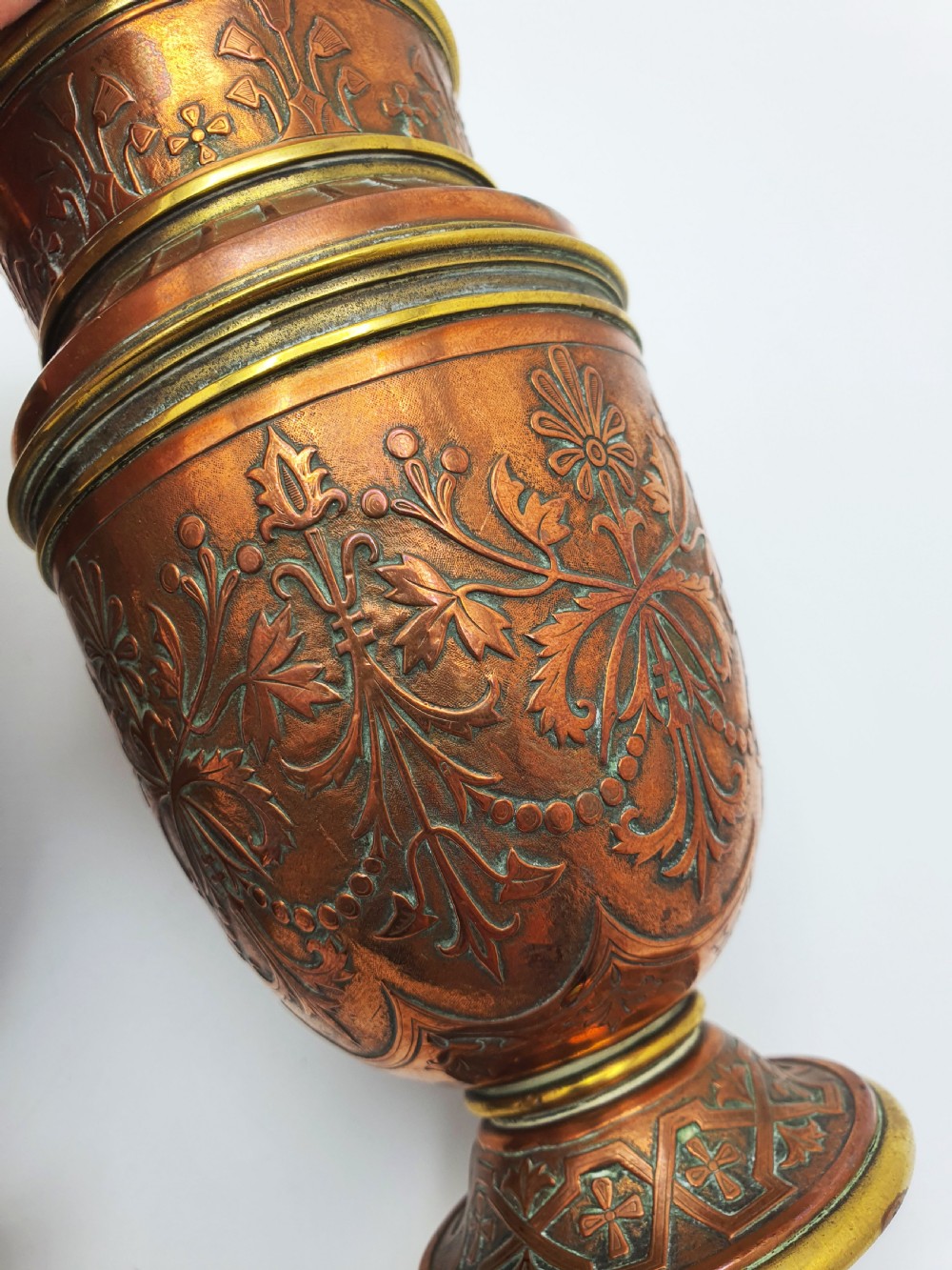 A pair of antique French copper urns featuring brass rims, pedestal bases, and chased floral motifs. View VII