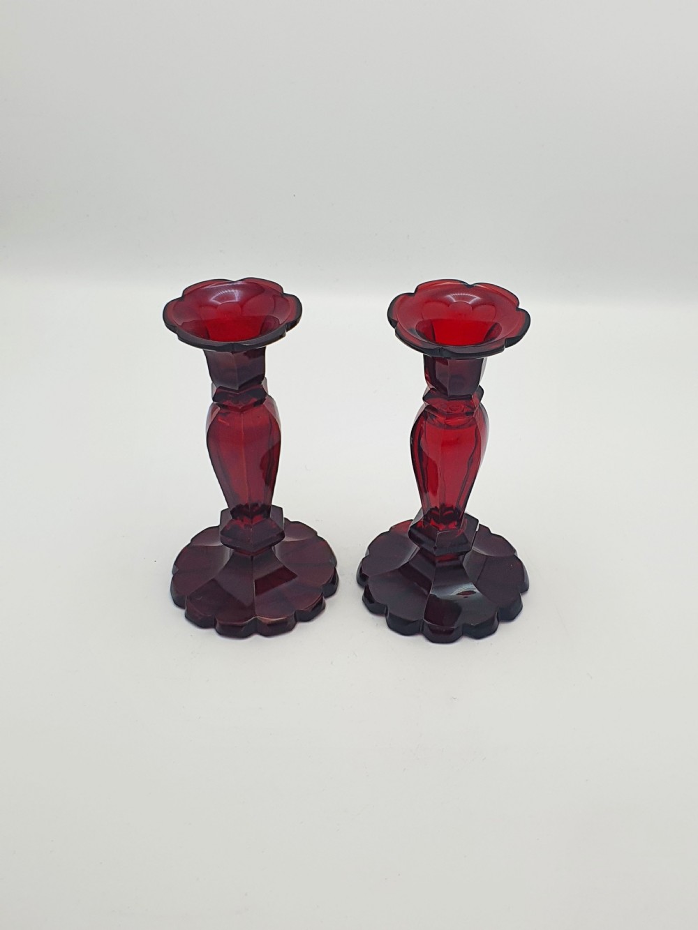 A pair of late 19th-century Continental ruby red cut glass candlesticks featuring faceted stems and scalloped bases.