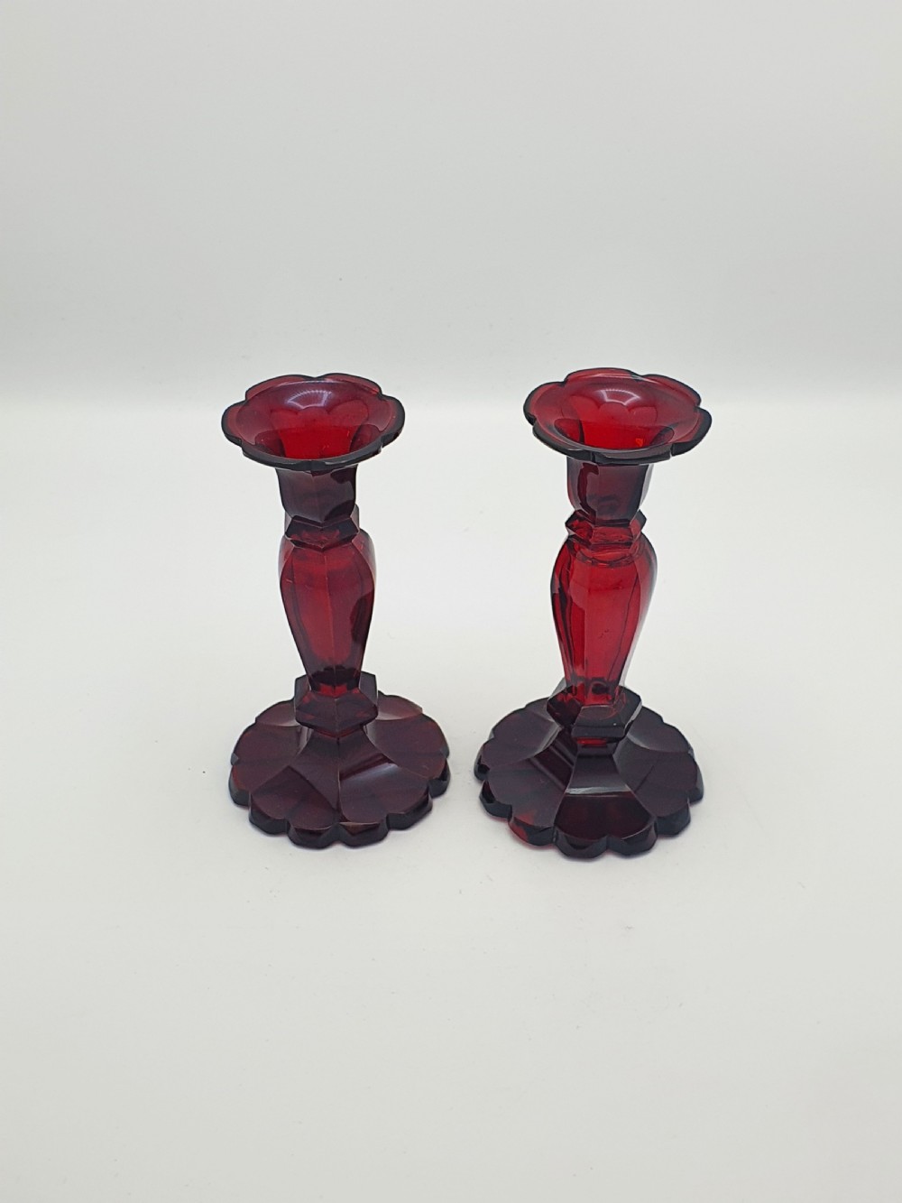 A pair of late 19th-century Continental ruby red cut glass candlesticks featuring faceted stems and scalloped bases. View II