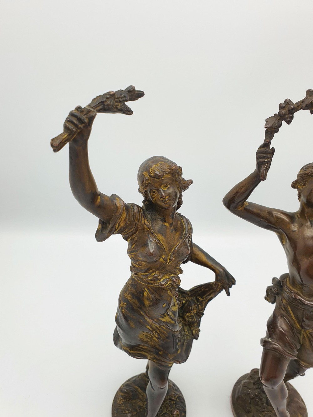 A pair of dark patinated bronze figurines depicting male and female harvest dancers holding floral garlands. View II
