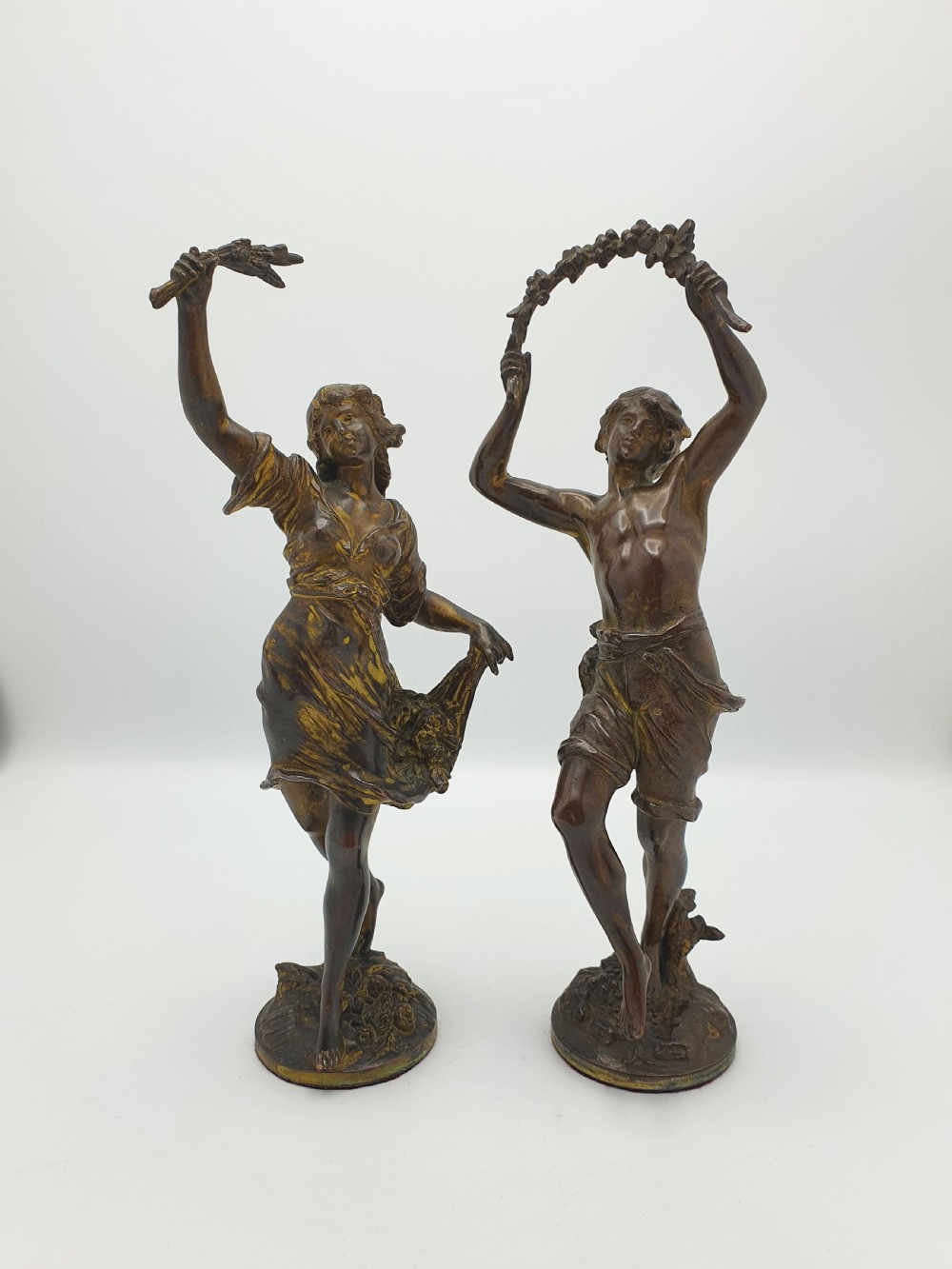 A pair of dark patinated bronze figurines depicting male and female harvest dancers holding floral garlands. View V
