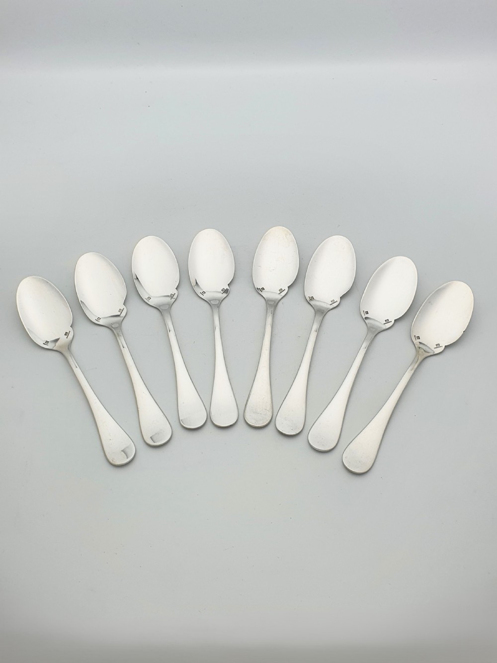 A set of eight French silver-plated dessert spoons arranged in a fan shape against a neutral background.
