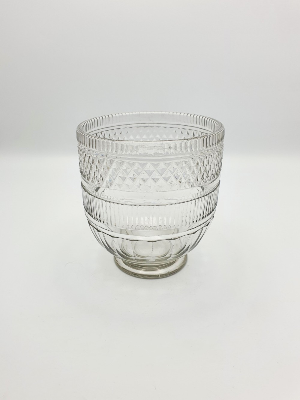 A Georgian cut clear glass tea mixing bowl featuring diamond cut patterns, step-cut bands, and a footed base.