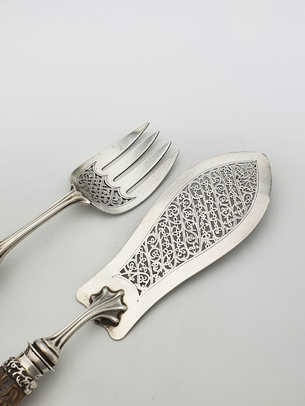A pair of Victorian silver fish servers featuring intricately engraved pierced blades and natural stag antler handles. View III