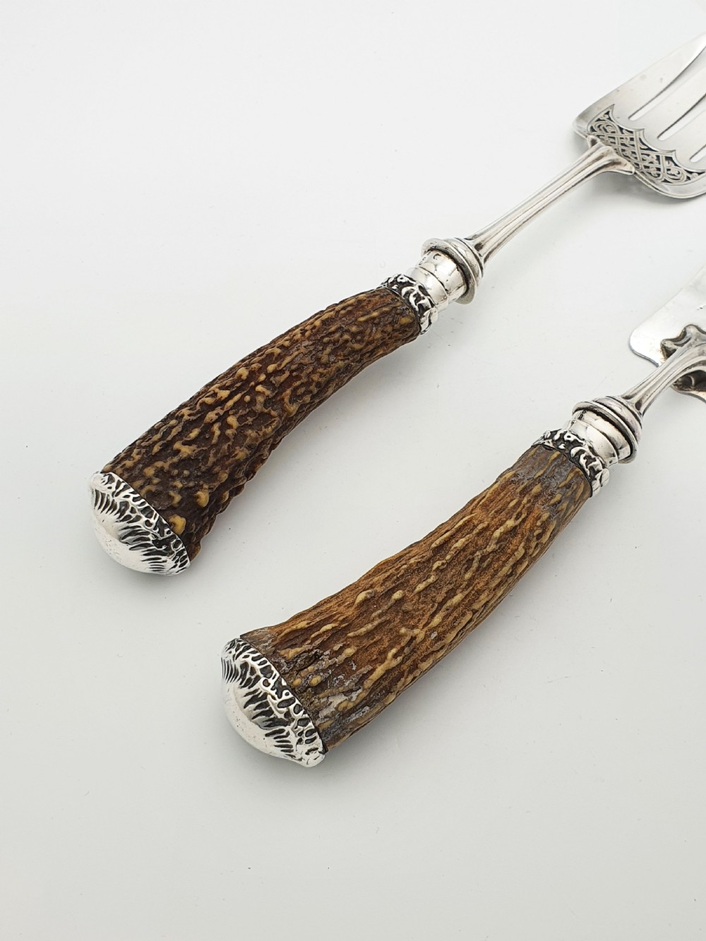 A pair of Victorian silver fish servers featuring intricately engraved pierced blades and natural stag antler handles. View V