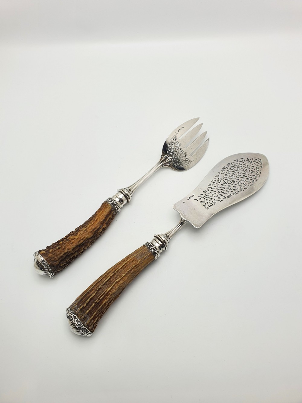A pair of Victorian silver fish servers featuring intricately engraved pierced blades and natural stag antler handles. View VI