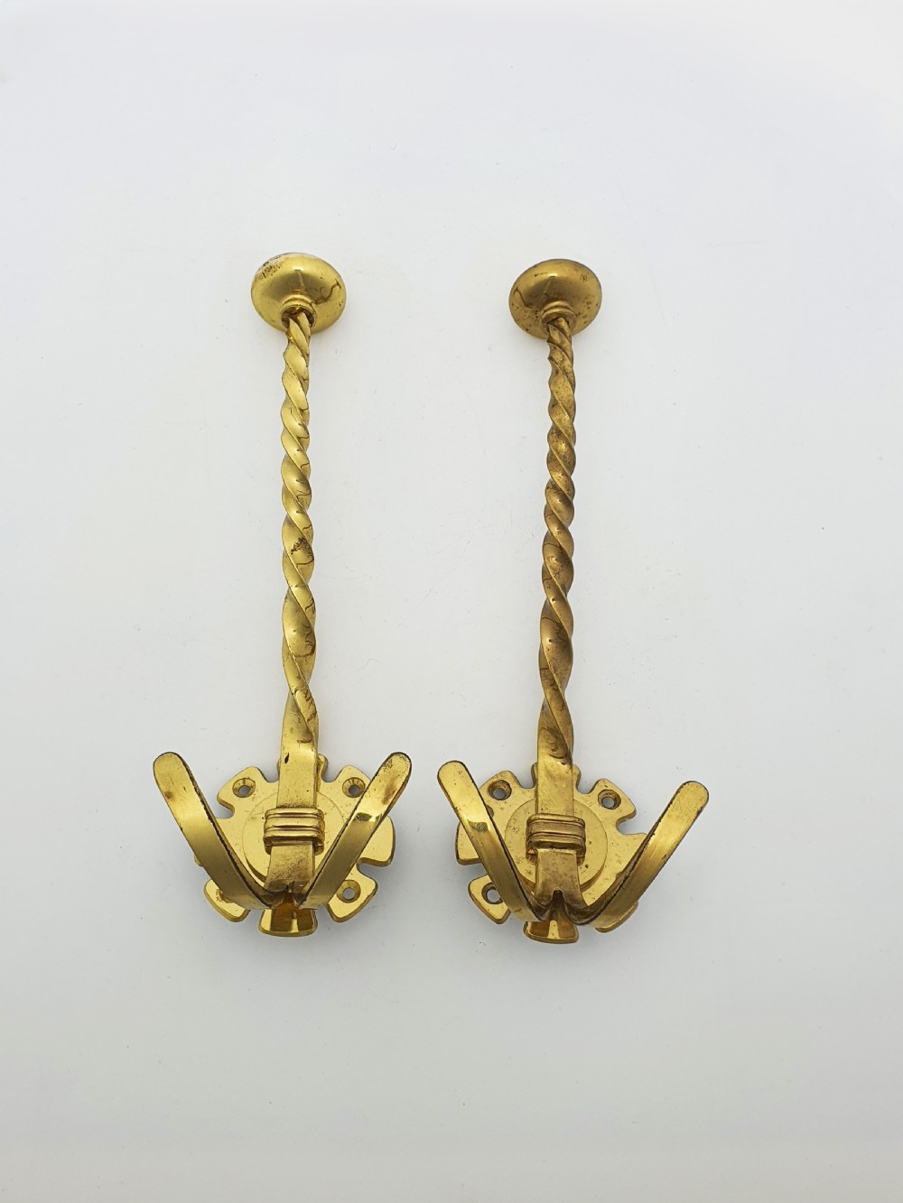 A pair of antique Victorian brass coat hooks with barley twist stems and multi-prong bases.