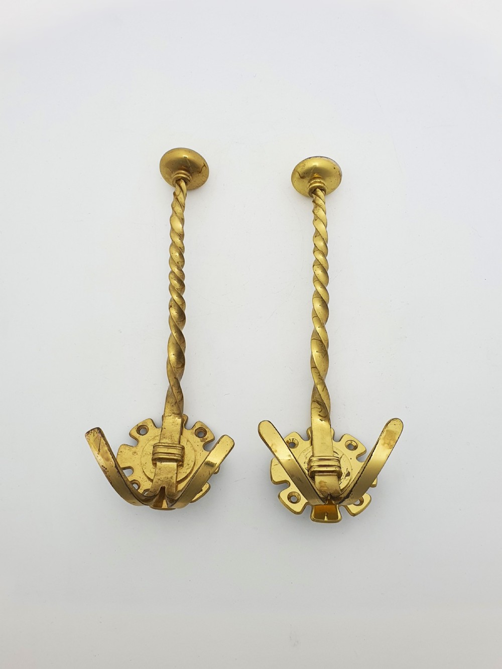 A pair of Victorian brass coat hooks featuring twisted central stems, circular mounting backplates, and curved double prongs.