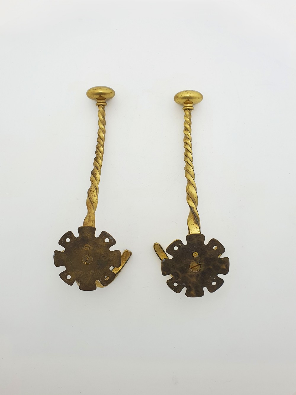 A pair of Victorian brass coat hooks featuring twisted central stems, circular mounting backplates, and curved double prongs. View II