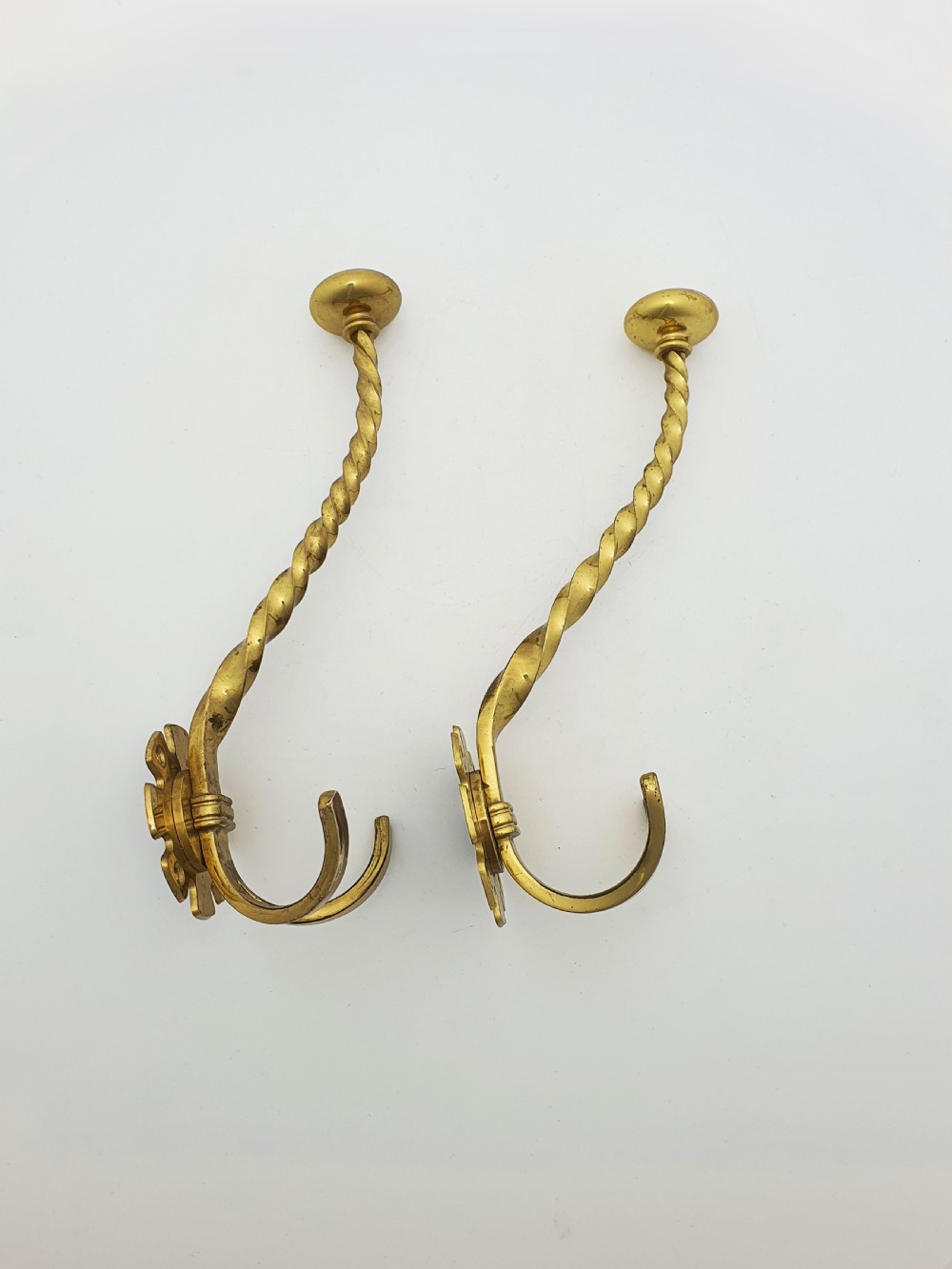 A pair of Victorian brass coat hooks featuring twisted central stems, circular mounting backplates, and curved double prongs. View III