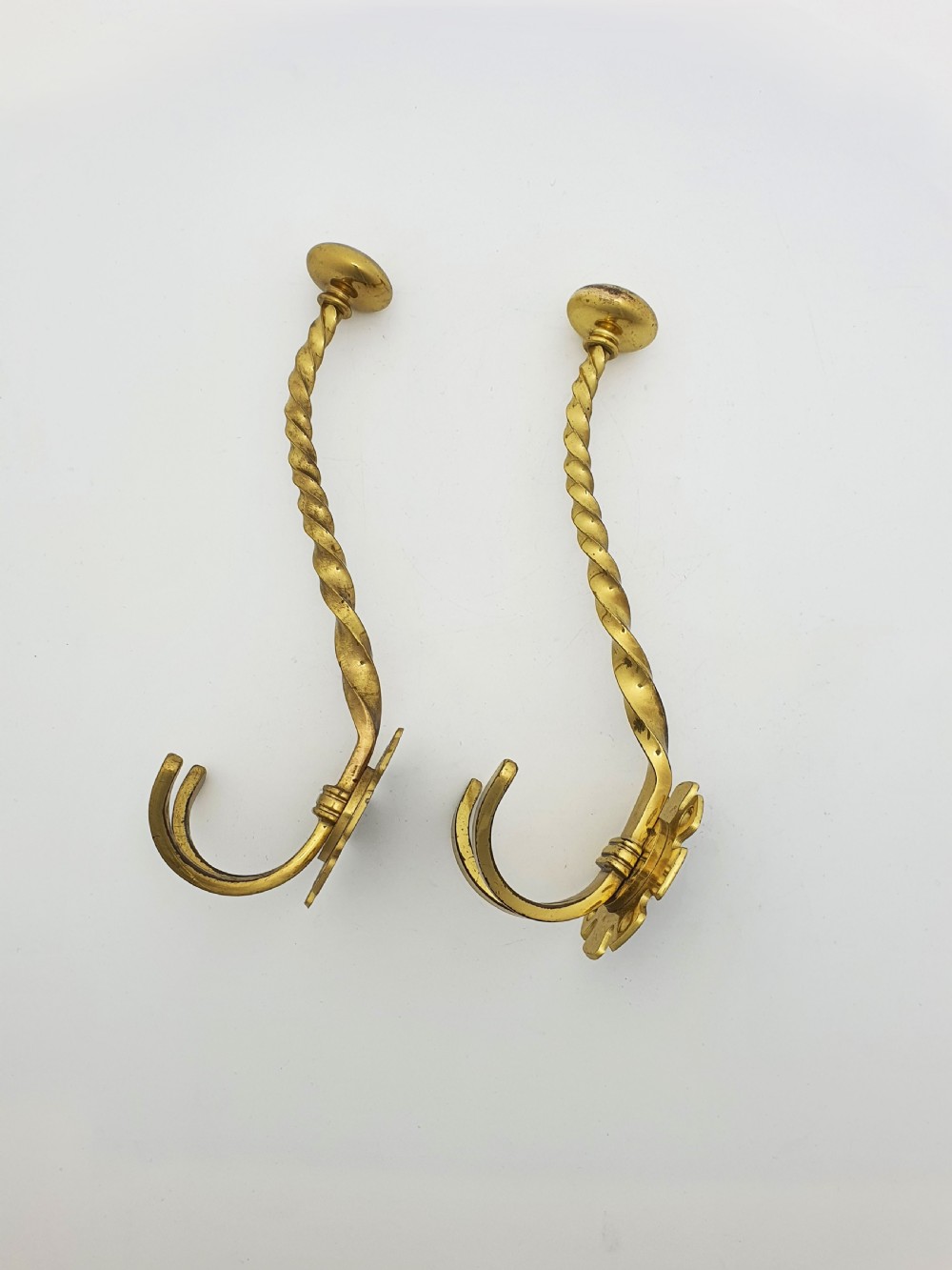 A pair of Victorian brass coat hooks featuring twisted central stems, circular mounting backplates, and curved double prongs. View IV