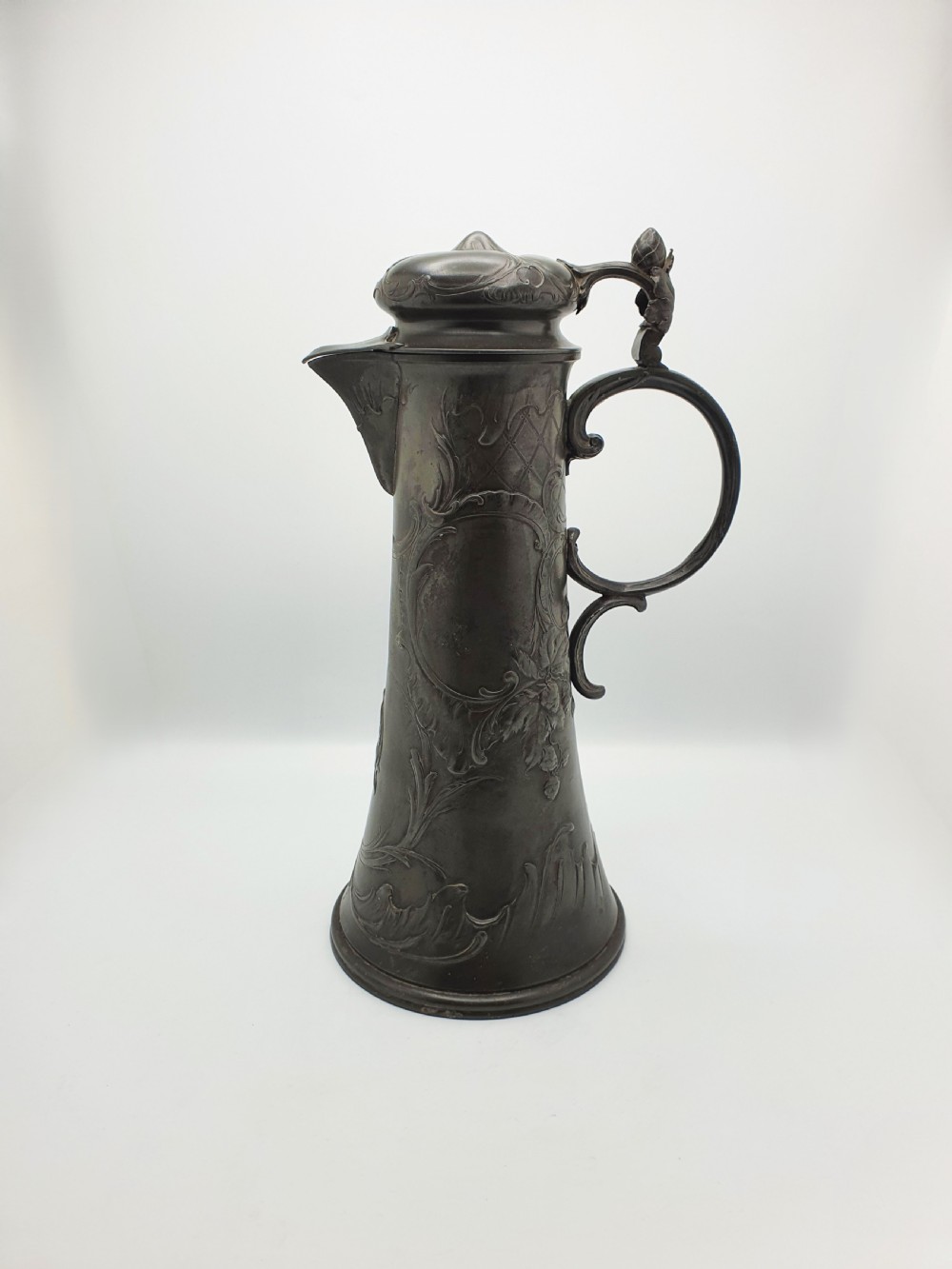 A tall German Art Nouveau pewter beer flagon featuring relief hops decoration, a flared base, a hinged lid, and a sweeping curved handle.