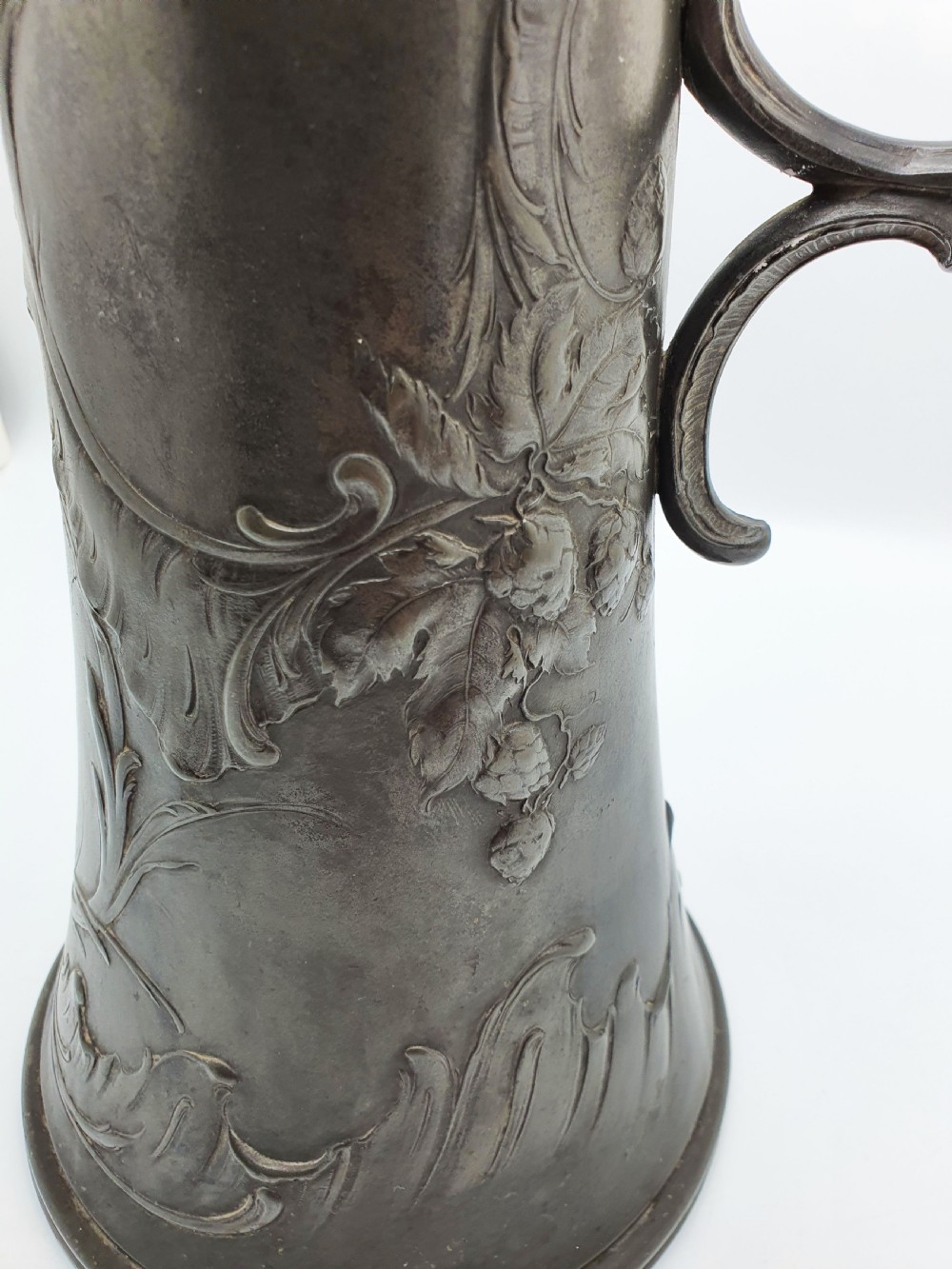 A tall German Art Nouveau pewter beer flagon featuring relief hops decoration, a flared base, a hinged lid, and a sweeping curved handle. View VI