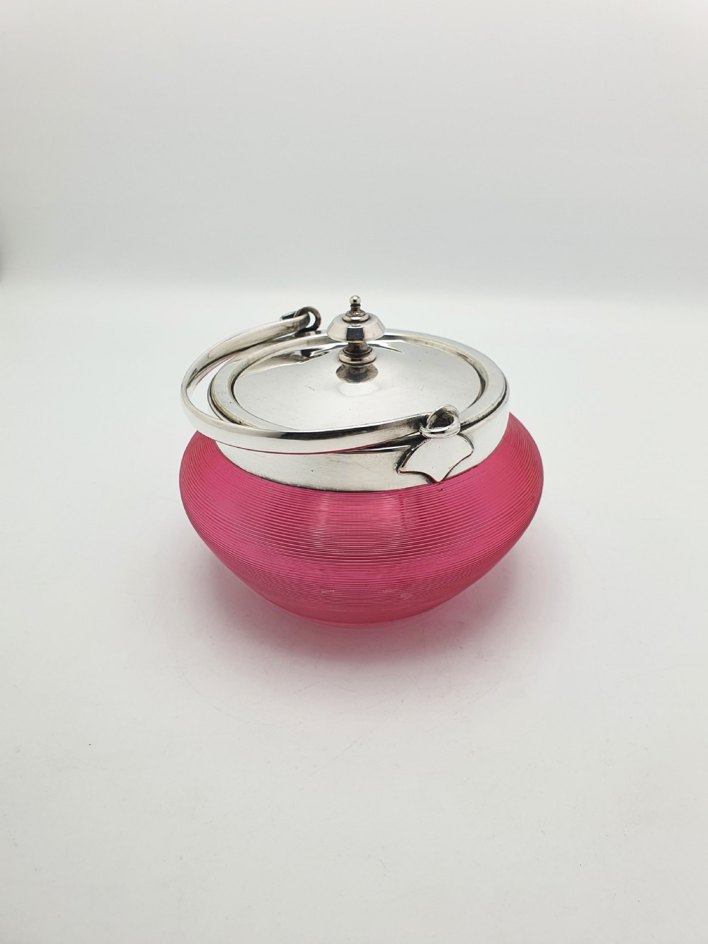 A ribbed cranberry glass biscuit barrel featuring a silver-plated fitted rim, flat lid, and hinged swing handle. View II