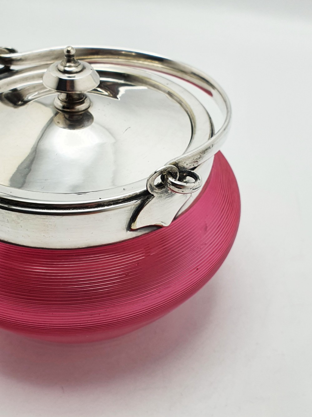 A ribbed cranberry glass biscuit barrel featuring a silver-plated fitted rim, flat lid, and hinged swing handle. View III