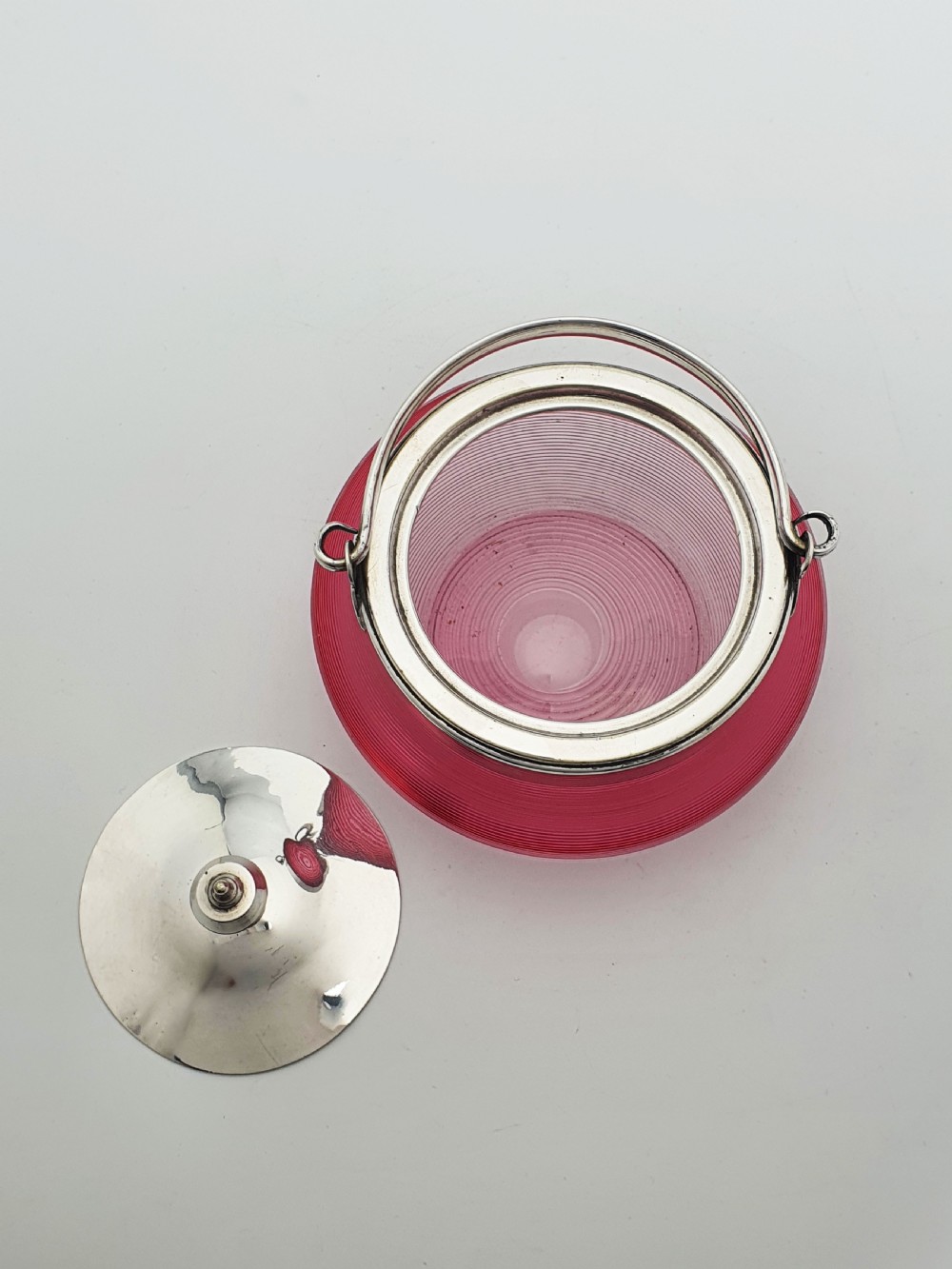A ribbed cranberry glass biscuit barrel featuring a silver-plated fitted rim, flat lid, and hinged swing handle. View VI