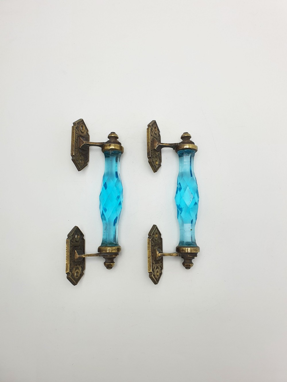 A pair of antique door handles featuring faceted blue glass grips supported by ornate brass mounting plates.