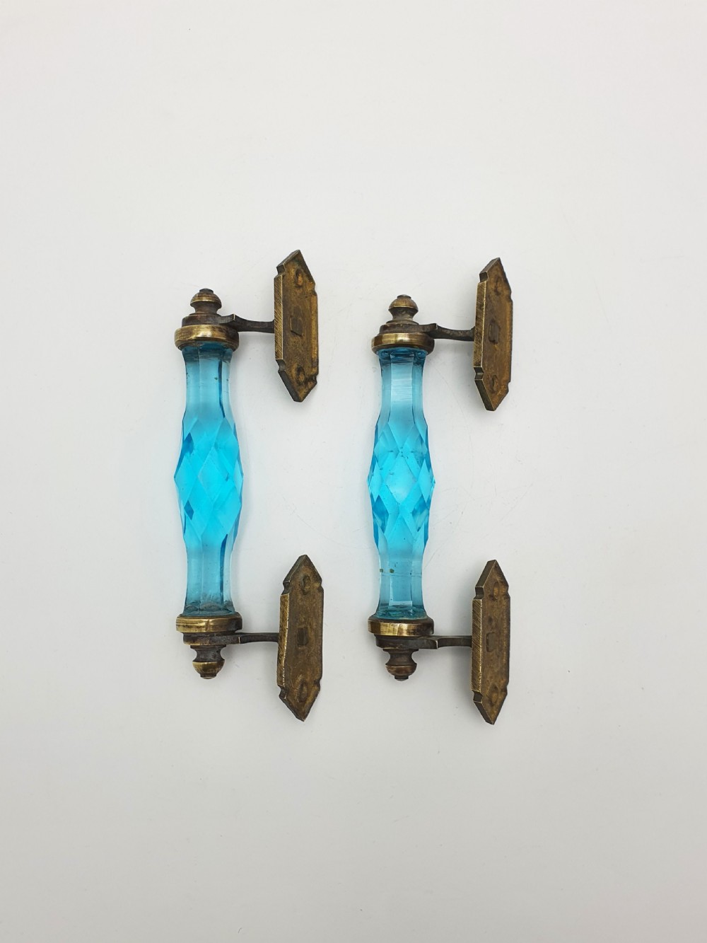 A pair of antique door handles featuring faceted blue glass grips supported by ornate brass mounting plates. View II