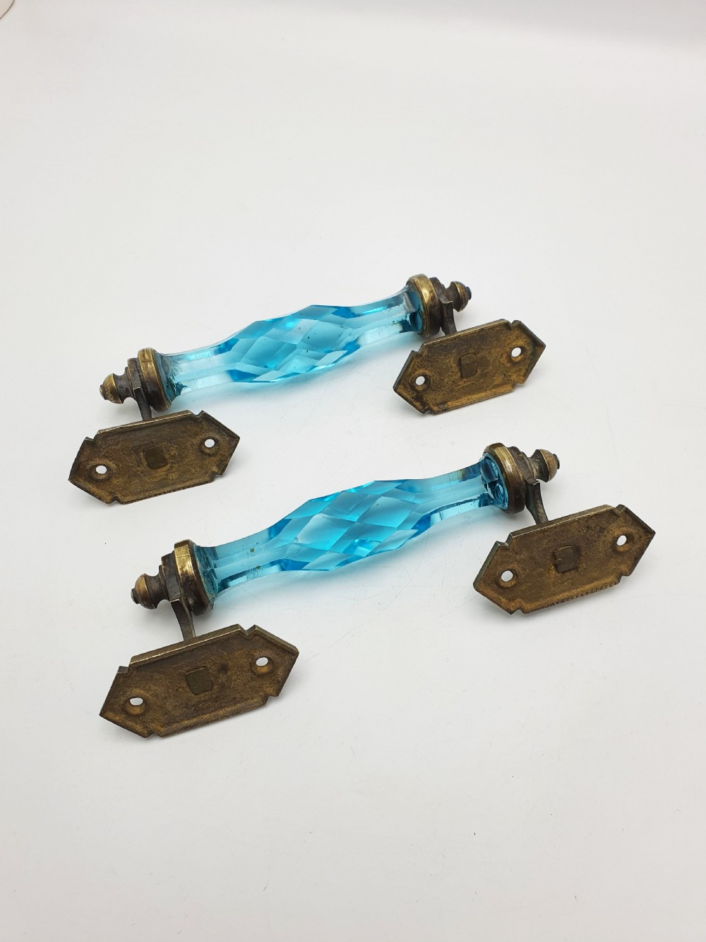 A pair of antique door handles featuring faceted blue glass grips supported by ornate brass mounting plates. View III