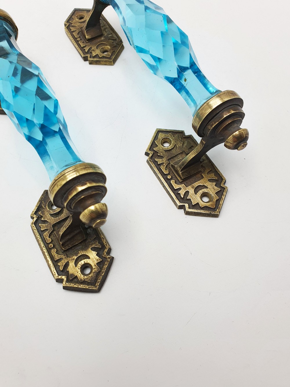 A pair of antique door handles featuring faceted blue glass grips supported by ornate brass mounting plates. View V