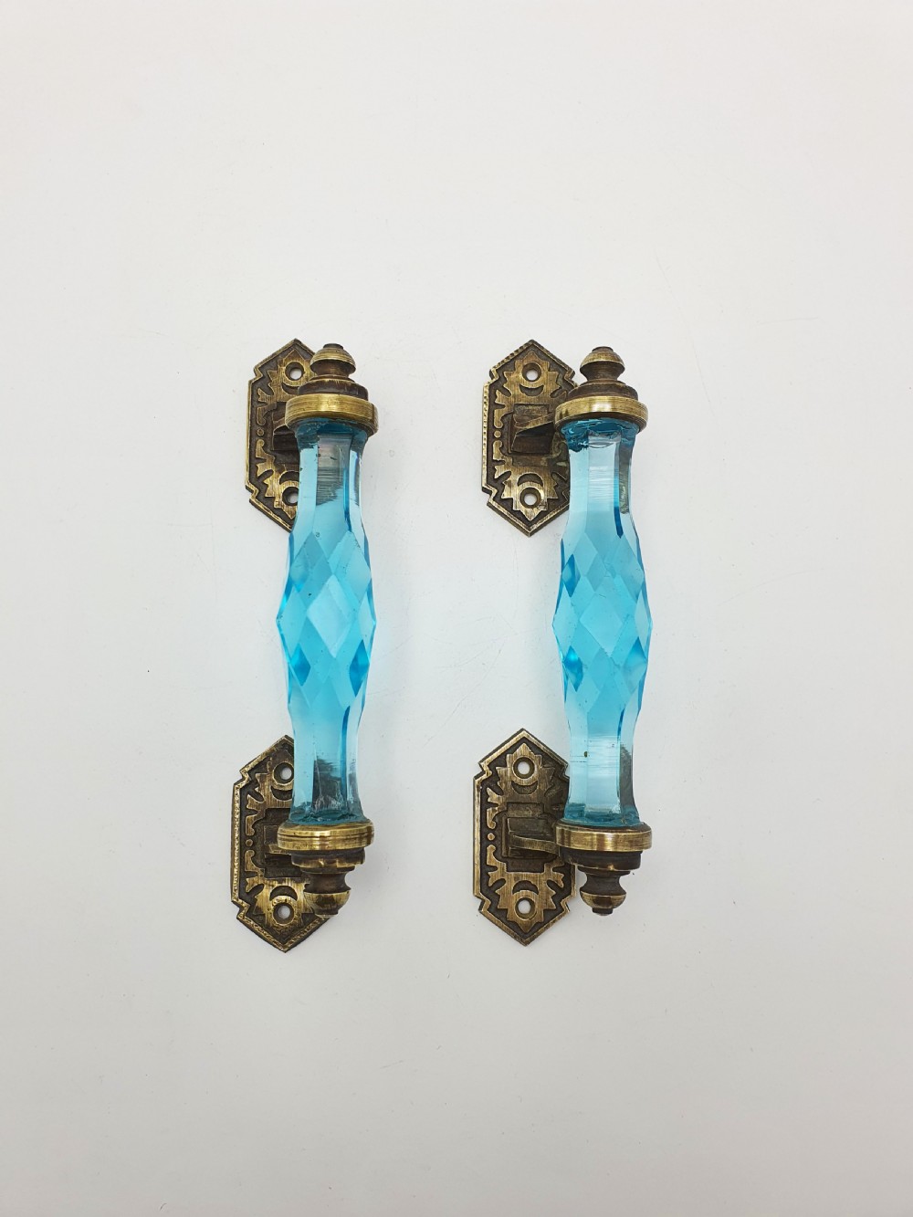 A pair of antique door handles featuring faceted blue glass grips supported by ornate brass mounting plates. View VI