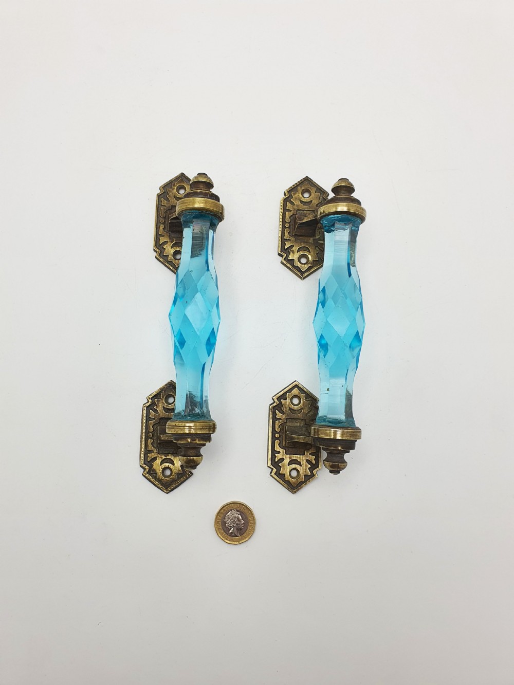A pair of antique door handles featuring faceted blue glass grips supported by ornate brass mounting plates. View VII
