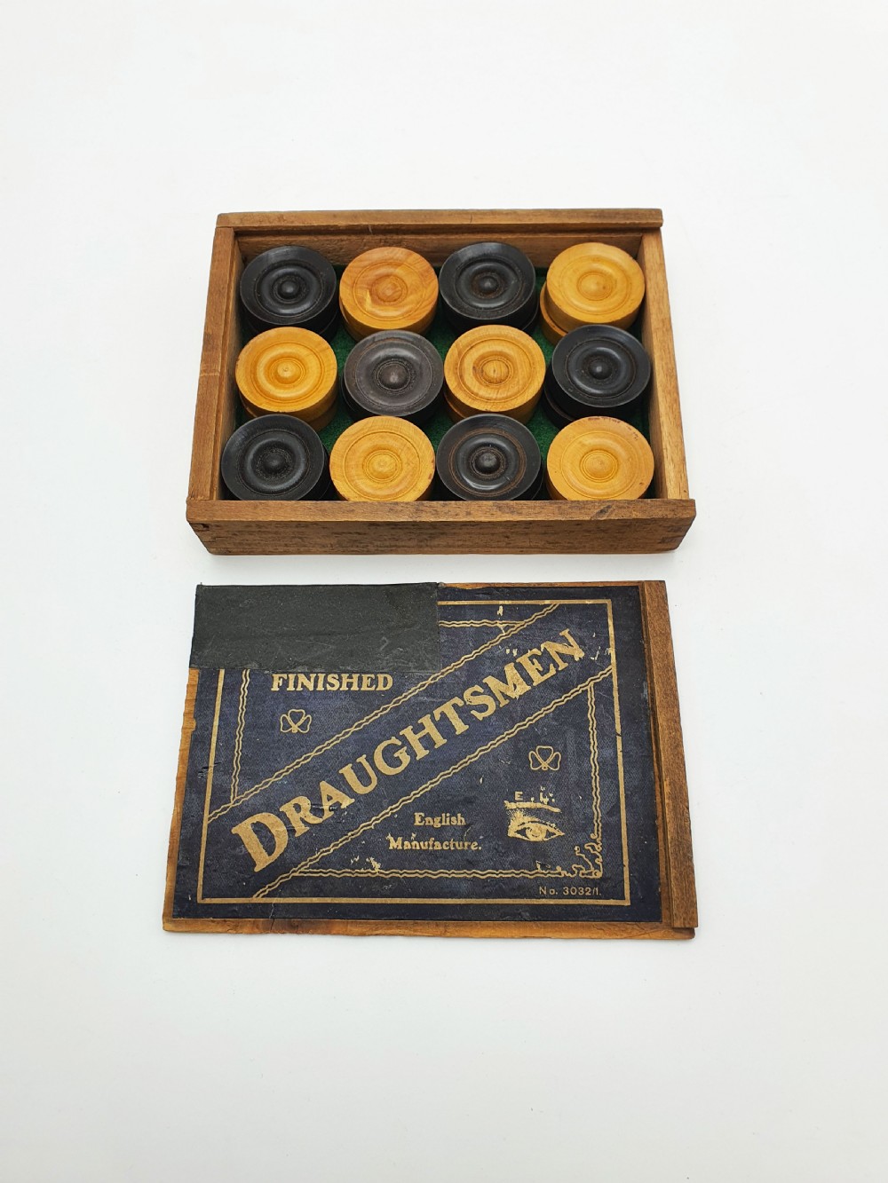 A set of turned boxwood and dark-stained wooden draughtsmen displayed in front of their original wooden slide-lid box with a printed label. View V