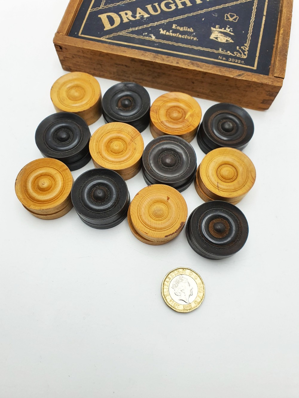 A set of turned boxwood and dark-stained wooden draughtsmen displayed in front of their original wooden slide-lid box with a printed label. View VII