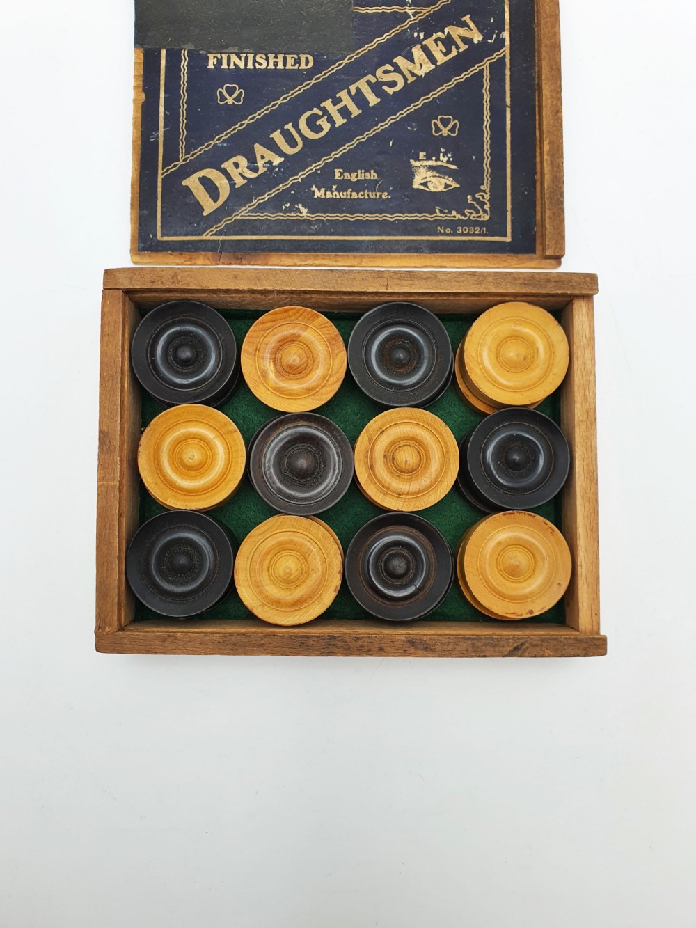A set of turned boxwood and dark-stained wooden draughtsmen displayed in front of their original wooden slide-lid box with a printed label. View VIII
