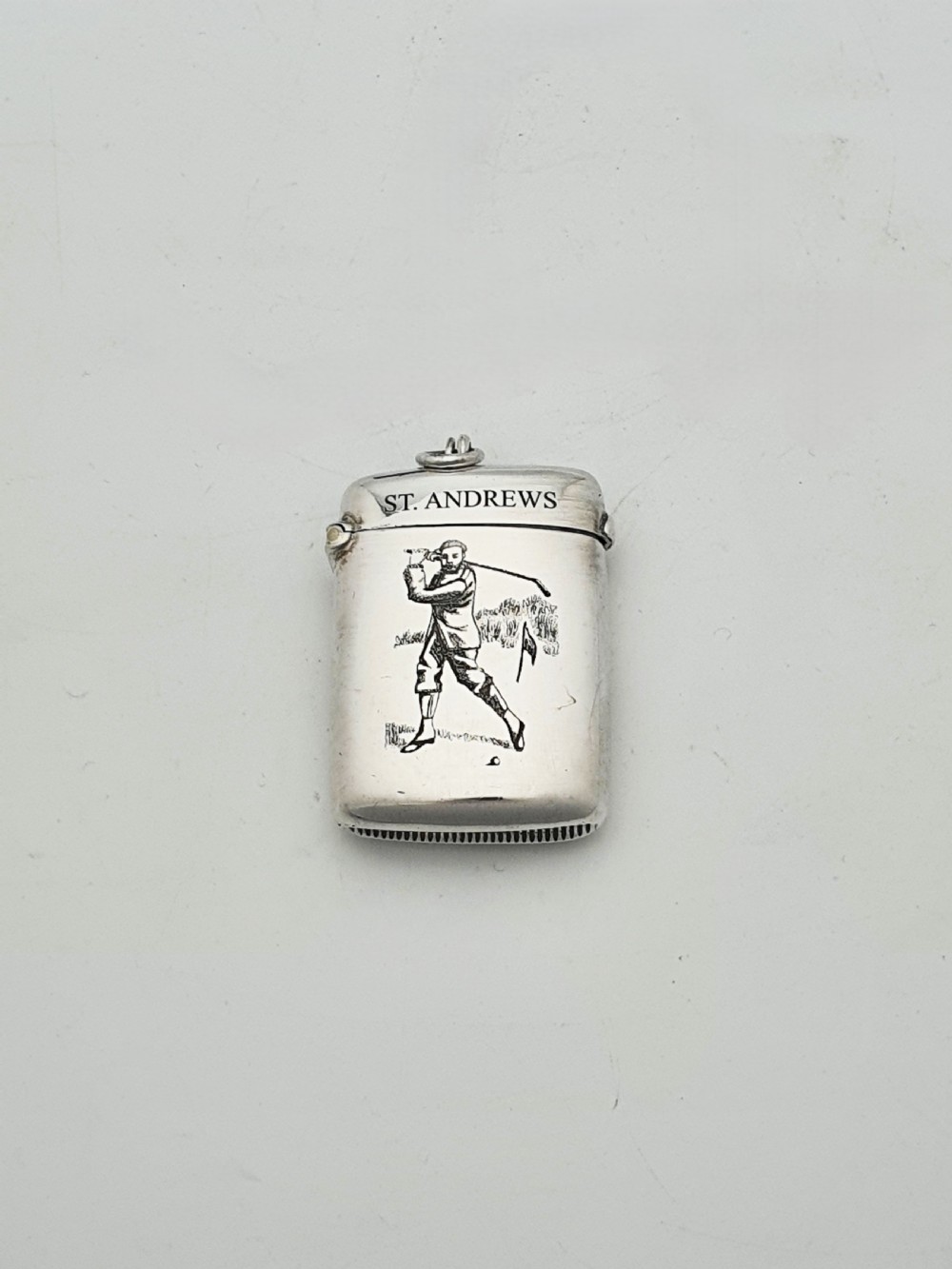 An antique sterling silver vesta case engraved with a golfer and St. Andrews lettering, displayed inside an open blue velvet box. View III