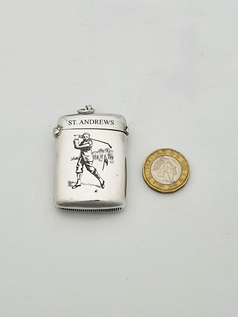 An antique sterling silver vesta case engraved with a golfer and St. Andrews lettering, displayed inside an open blue velvet box. View IX