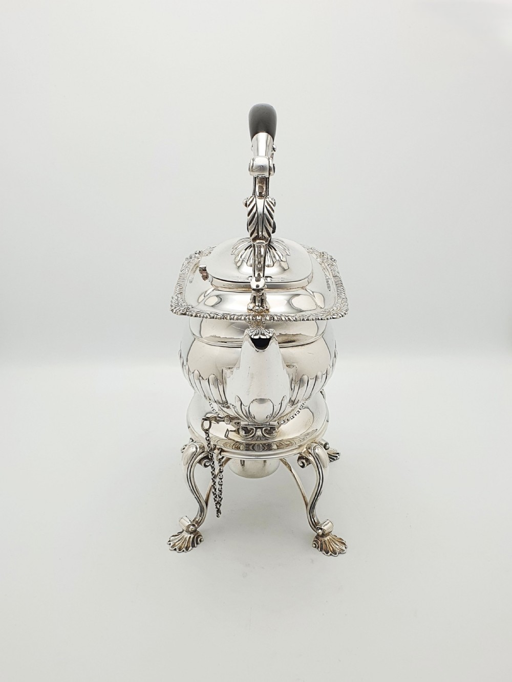 An antique Georgian-style silver-plated spirit kettle resting on a three-legged burner stand with shell feet and an ebony handle. View VI