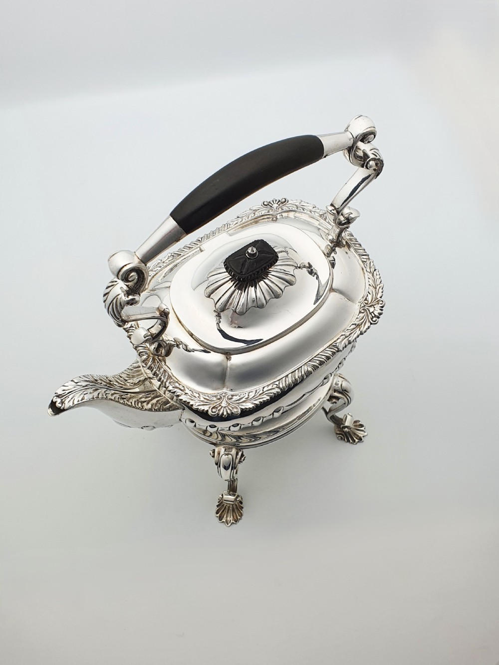 An antique Georgian-style silver-plated spirit kettle resting on a three-legged burner stand with shell feet and an ebony handle. View VII