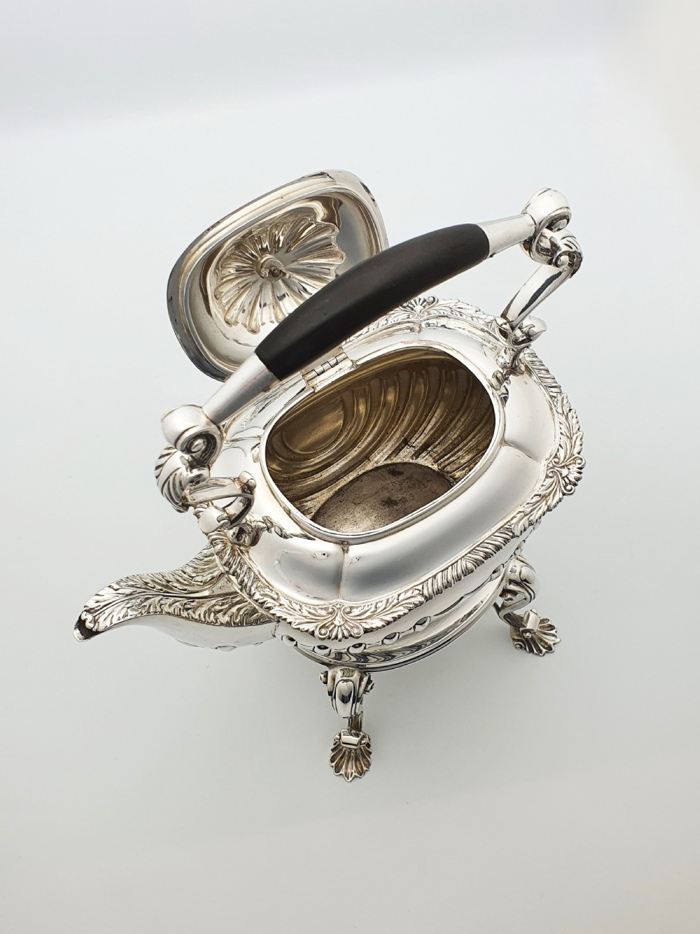 An antique Georgian-style silver-plated spirit kettle resting on a three-legged burner stand with shell feet and an ebony handle. View VIII