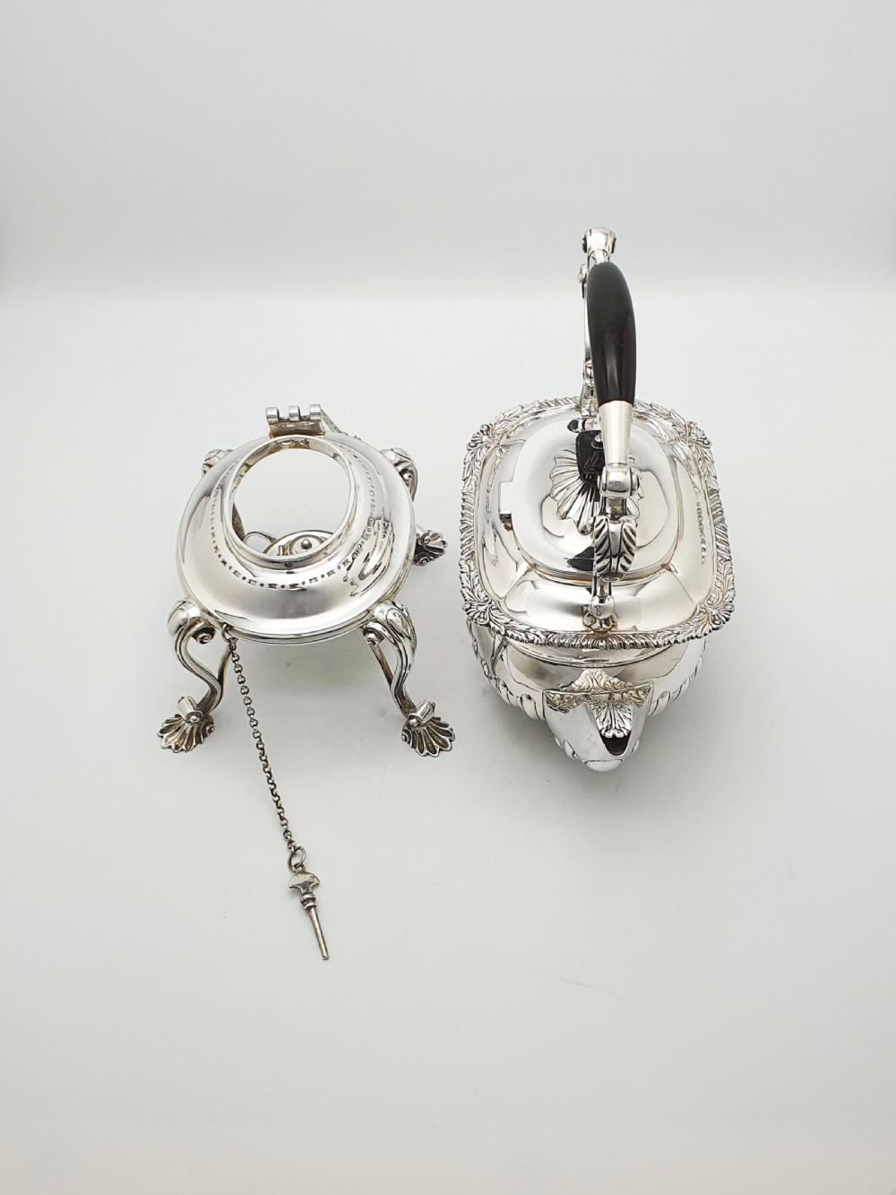 An antique Georgian-style silver-plated spirit kettle resting on a three-legged burner stand with shell feet and an ebony handle. View IX
