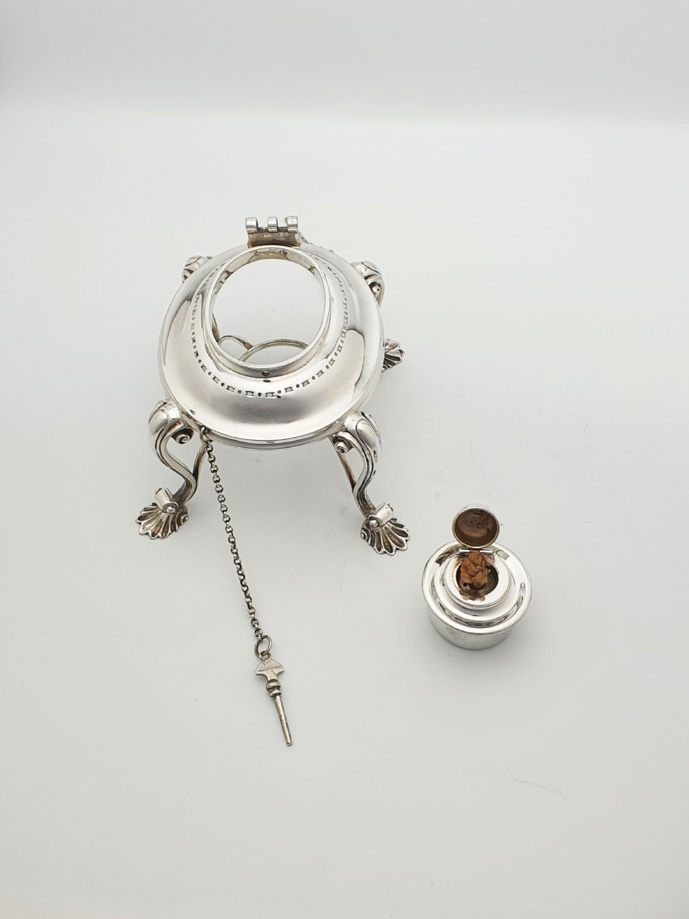 An antique Georgian-style silver-plated spirit kettle resting on a three-legged burner stand with shell feet and an ebony handle. View X