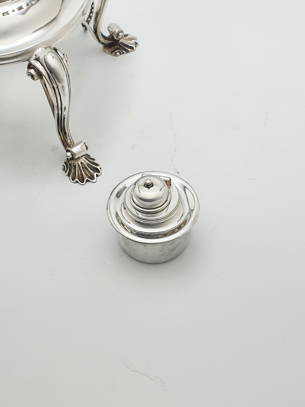 An antique Georgian-style silver-plated spirit kettle resting on a three-legged burner stand with shell feet and an ebony handle. View XI